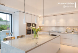 The vase with green flowers standing on the white kitchen island of a modern design.