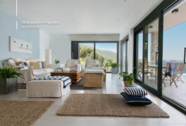 Open space white living room, surrounded with large windows and with white couch and brown carpets.