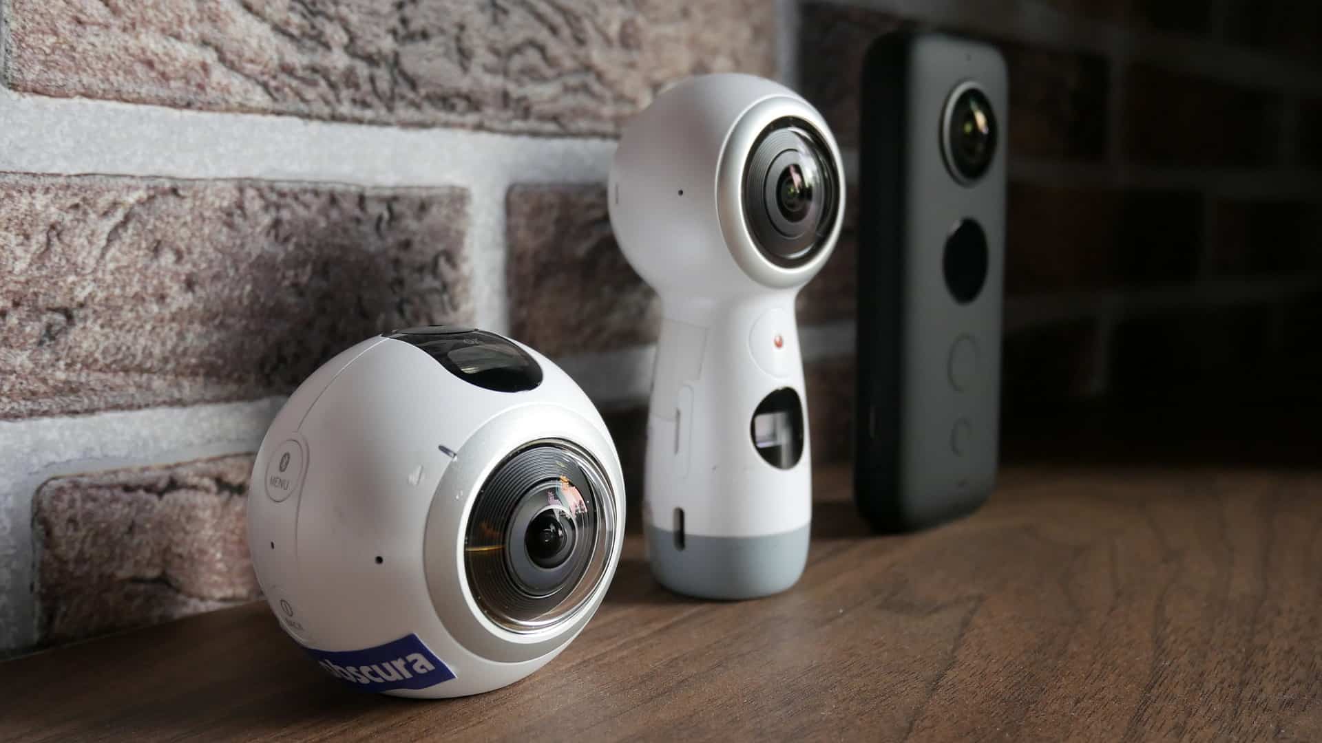 Three 360 cameras lined up on a wooden surface.