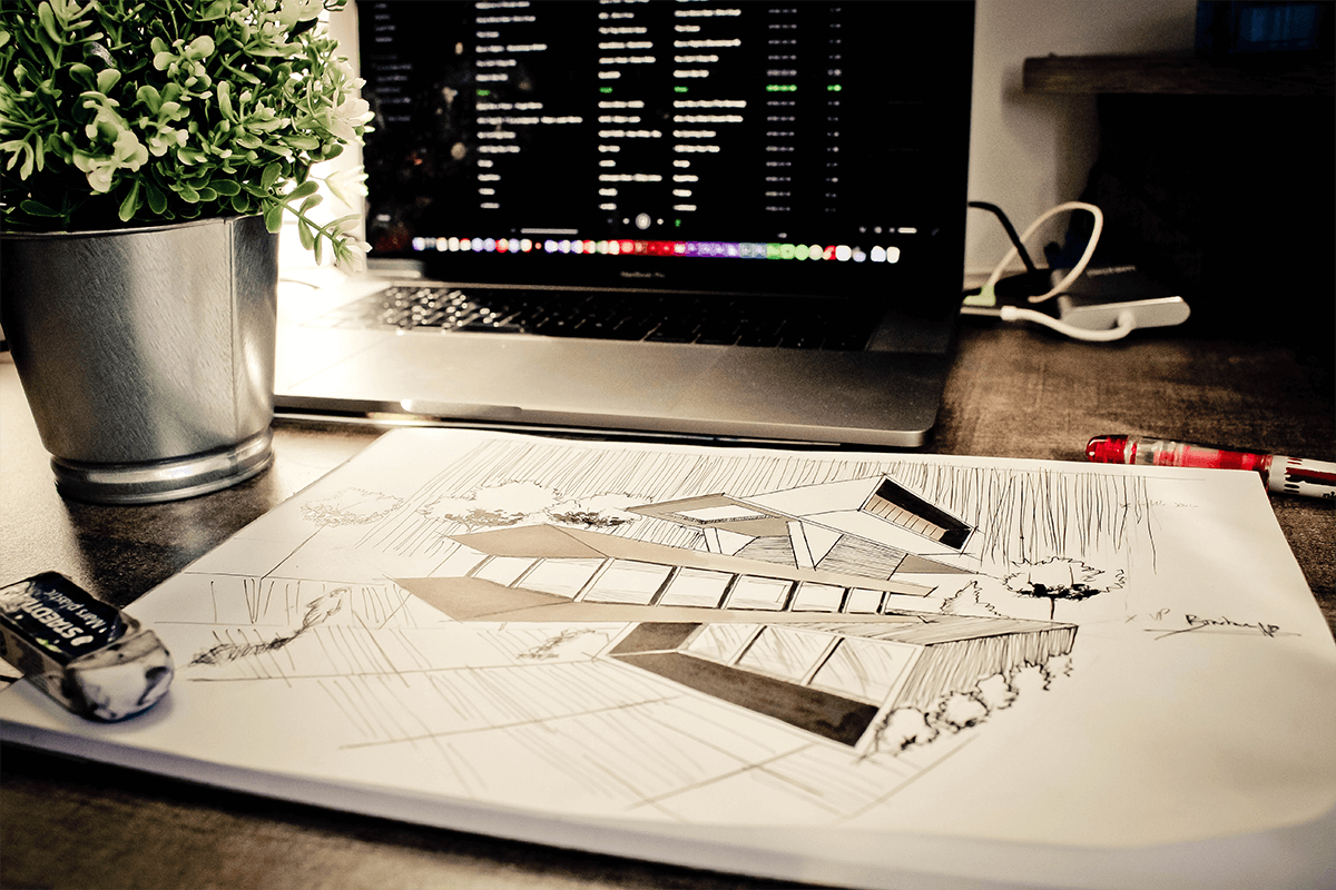 Working table with architectual drawings, laptop and flower on it.