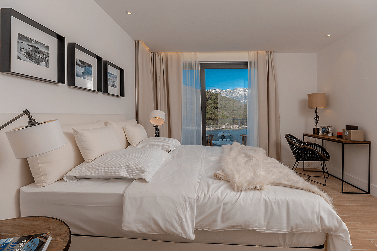 A white bed with white sheets and pillows in a modern designed bedromm with a sea view.