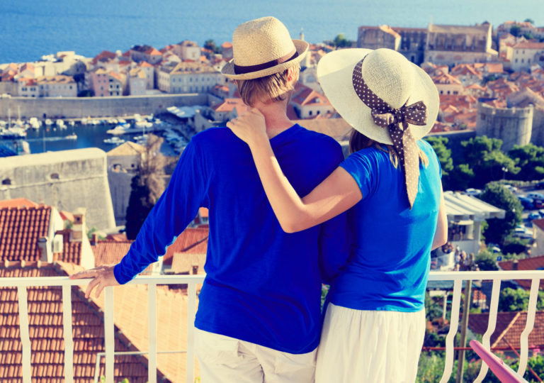 A couple in blue shirts and white hats looking at the city from the viewpoint.