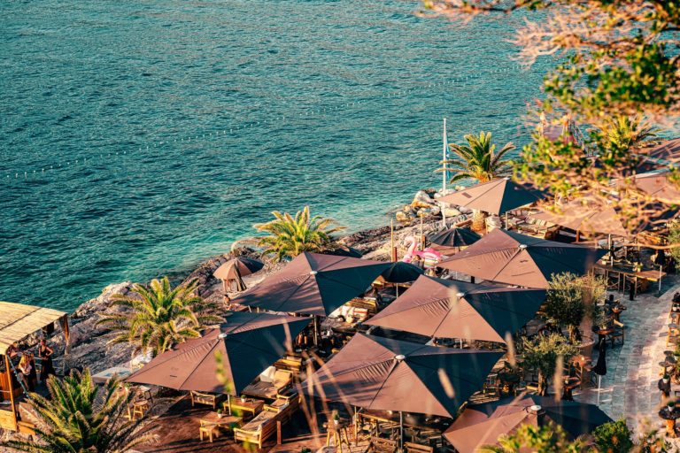 Seven brown parasols in the beach bar, surrounded with green palm trees.