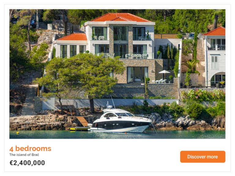 The luxury seafront mansion with a huge floor to ceiling glass window in the middle. The white yacht is moored in front of the mansion.