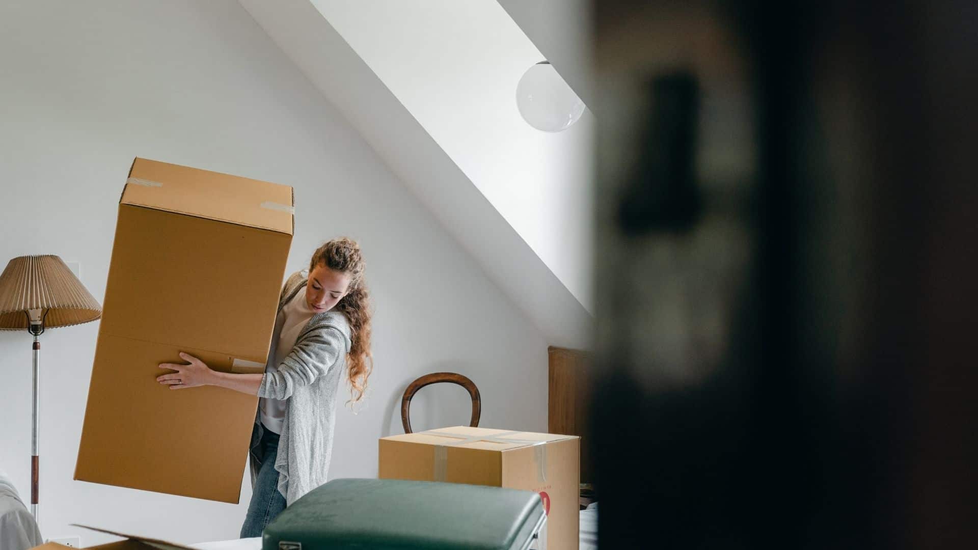 A woman in the living room packing personal things in the boxes for moving purposes.