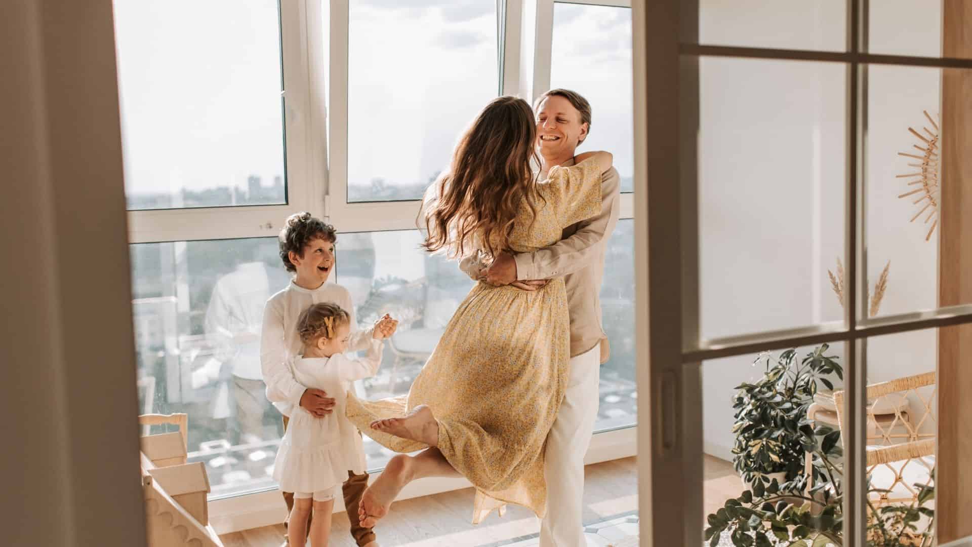 Husband and wife hugged in front of their happy children in the house.