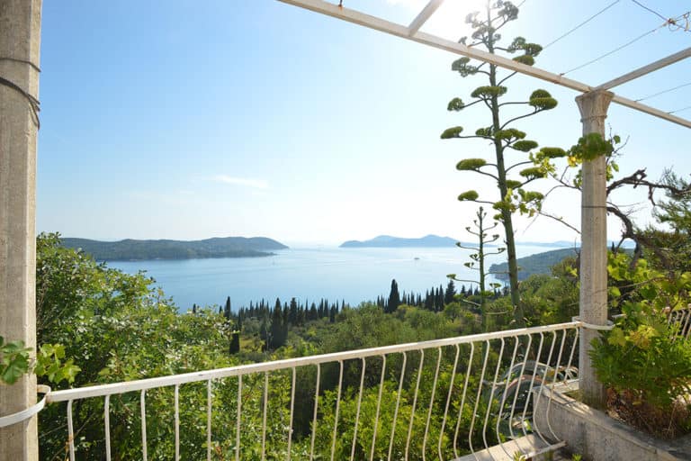 The balcony with a view on the cypress trees, blue sea, and the island in the distance.