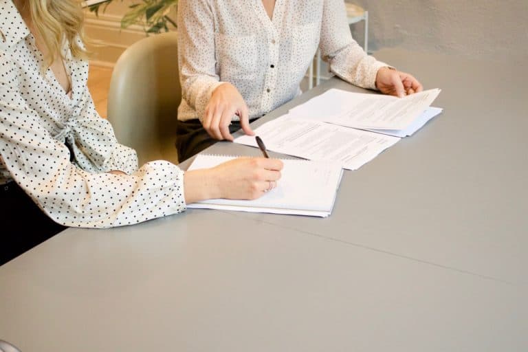 Two women in white shirts signing a contract on the grey tabel.