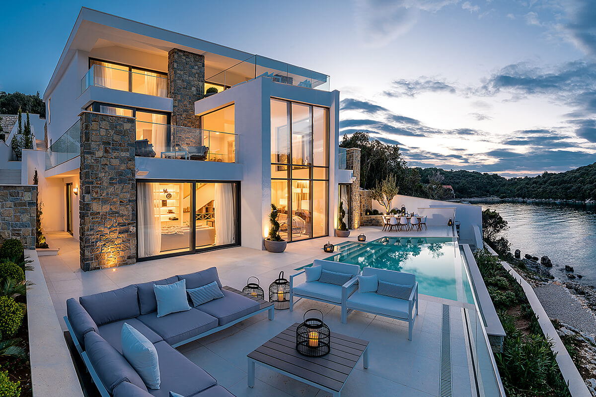 White waterfront villa with a swimming pool in the evening.