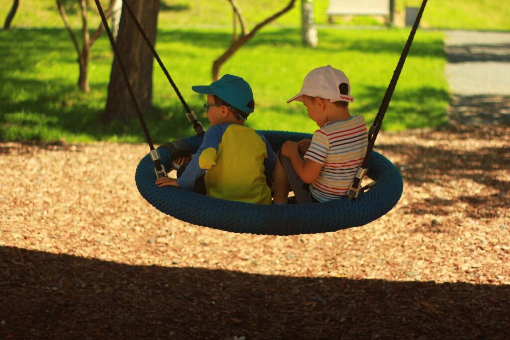 Two kids on a swing in the park.