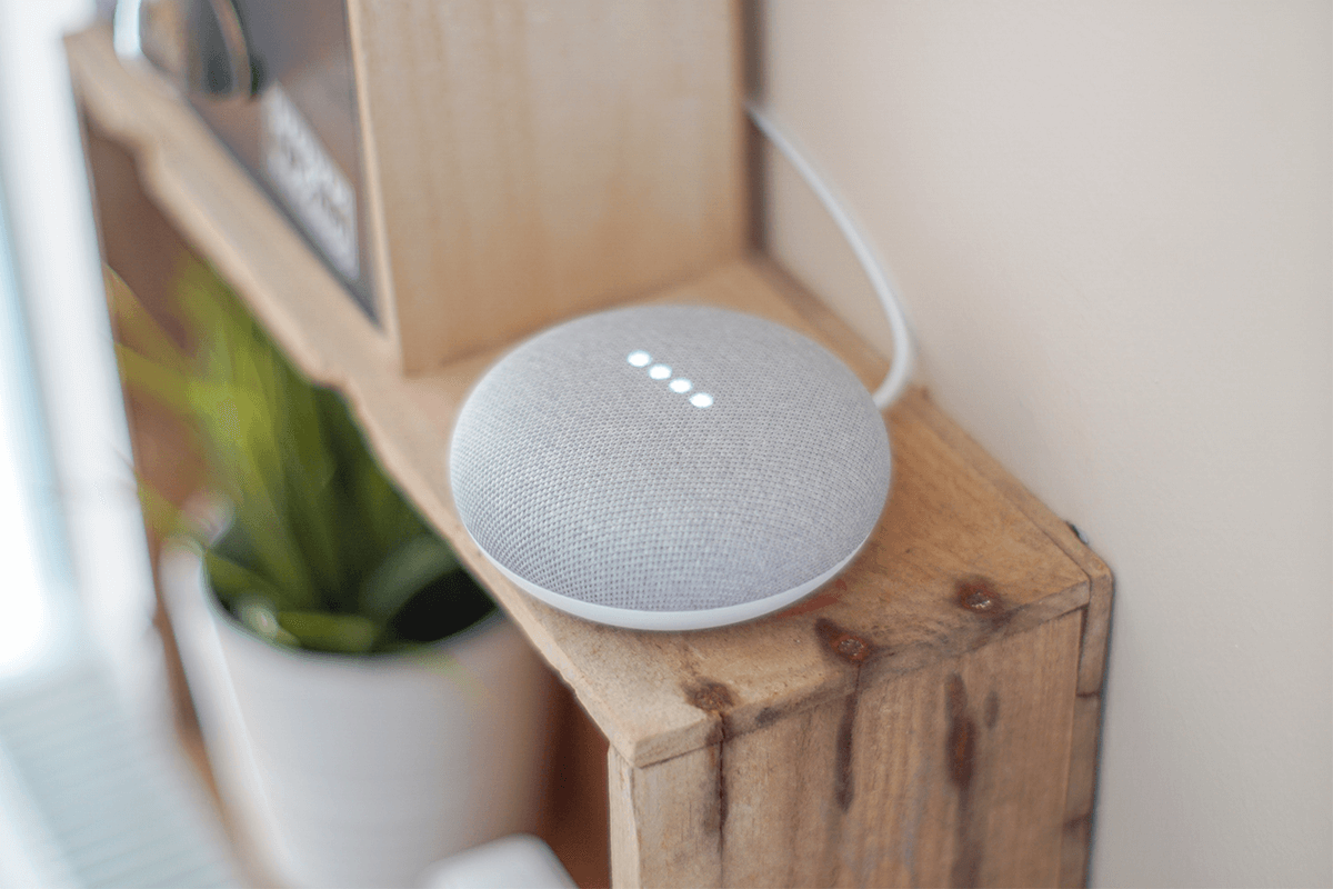A gray voice control gadget standing on a wooden shelf in a living room.