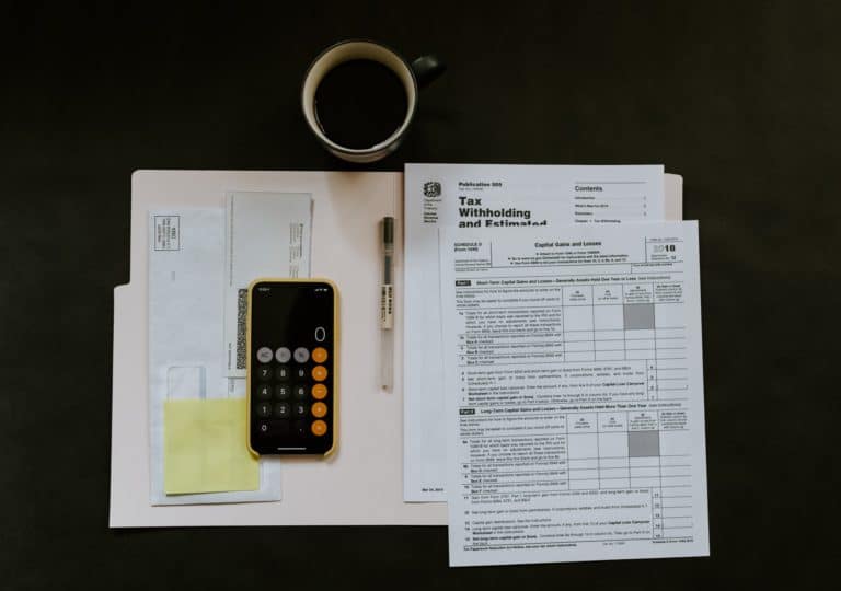 Tax papers and financial notes in the open notebook, and a black smartphone with a calculator app.