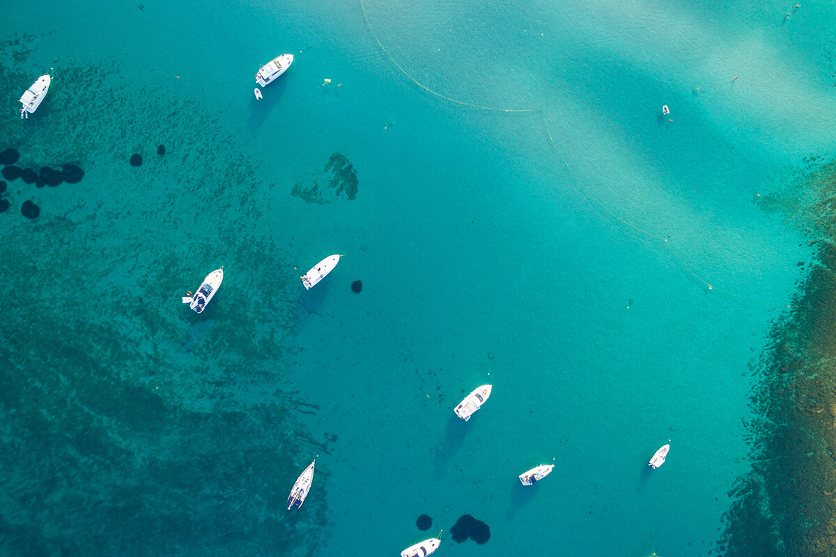 Nine white yachts sailing on a emerald blue sea, a image taken from bird's perspective.